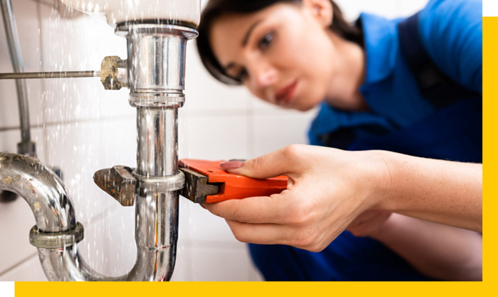 Female plumber with wrench working on leak under bathroom sink